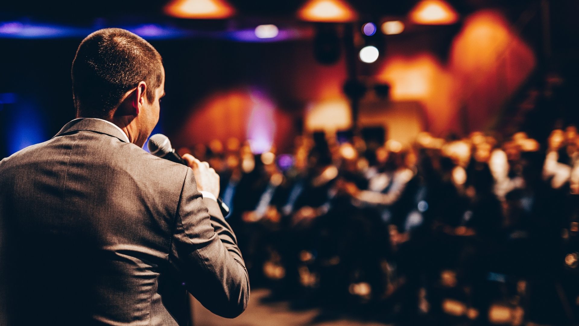 well dress business man on stage with a microphone speaking to the crowd